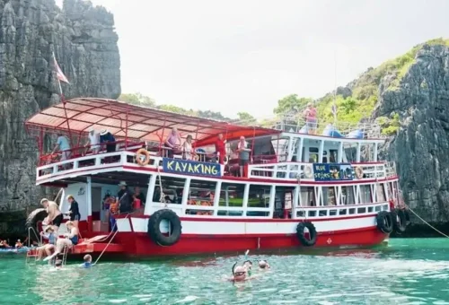 Tour boat anchored at Angthong Marine Park with visitors kayaking and snorkeling in turquoise waters.
