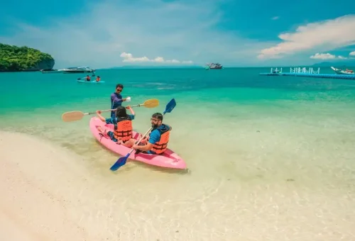 Tourists kayaking from a white sandy beach into turquoise waters at Angthong Marine Park.