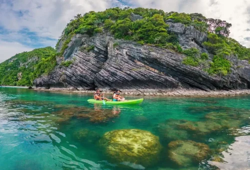 Visitors kayaking near limestone cliffs surrounded by emerald water in Angthong Marine Park.