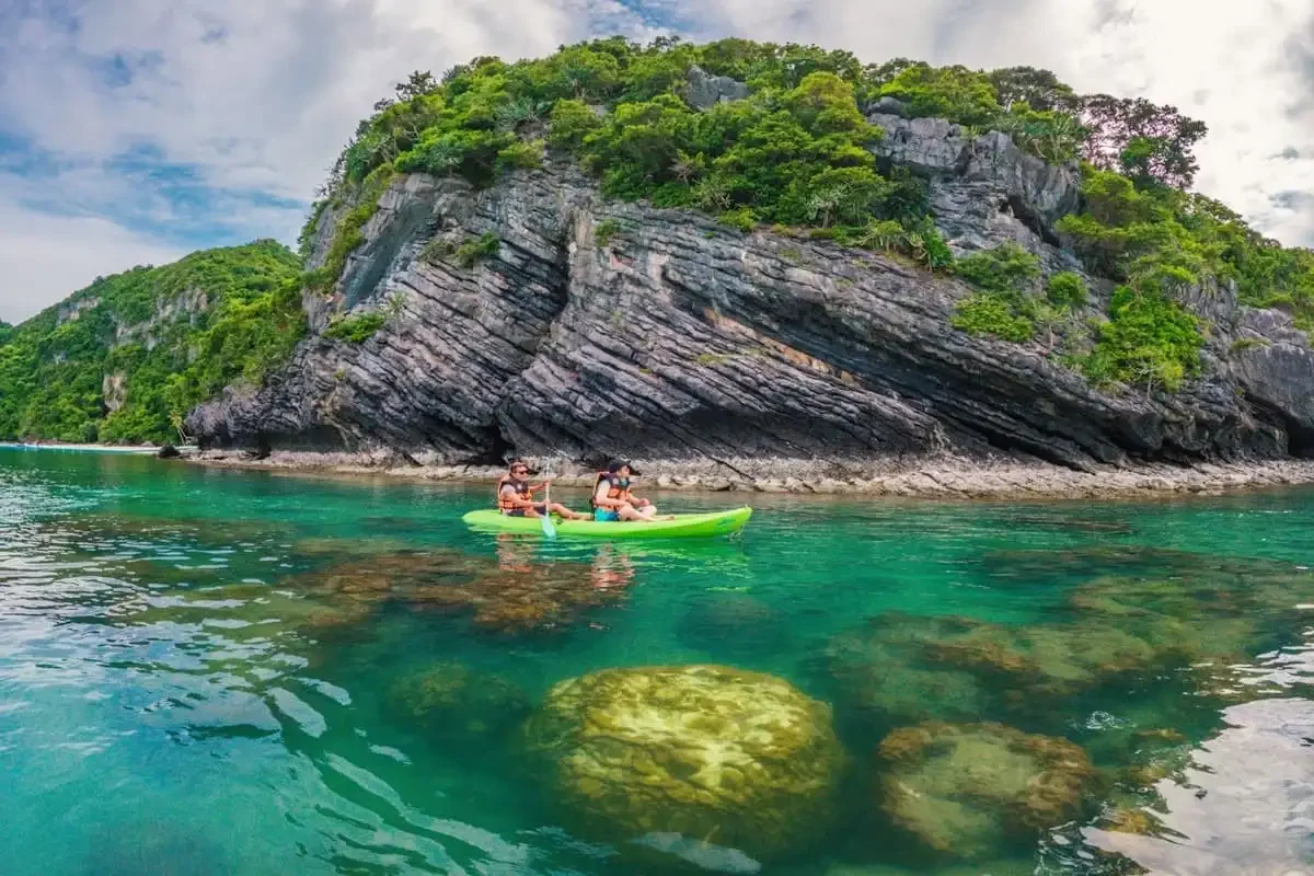 Visitors kayaking near limestone cliffs surrounded by emerald water in Angthong Marine Park.