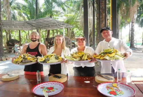 Group of travelers proudly holding trays of prepared elephant food at Krabi Elephant Shelter.