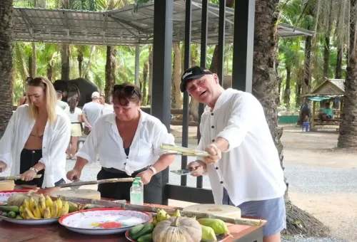 Tourists smiling while cutting sugarcane and vegetables for elephants at Krabi Elephant Shelter.