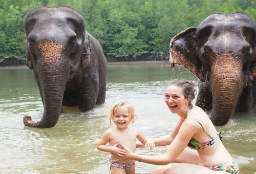 Mother and daughter playing with elephants in shallow water at Krabi Elephant Shelter.