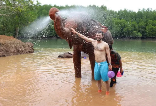 Elephant splashing water on a visitor during the bathing session at Krabi Elephant Shelter.