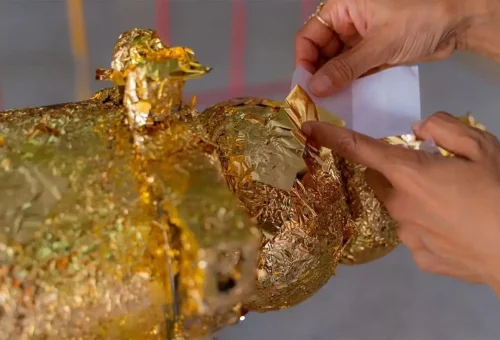 Private Phuket City Tour – visitor placing gold leaf on Buddha statue as part of traditional Thai merit ceremony with Phuket Travel Store.