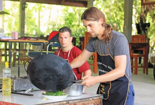 Traveler cooking Thai food using a wok at Ya’s Thai Cookery School Krabi with Phuket Travel Store.