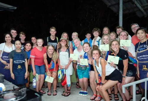 A large group of students proudly holding certificates after completing the Thai cooking class.