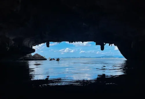 Kayaking out of a dark sea cave into a bright open ocean view in Phang Nga Bay on a James Bond private speedboat experience.