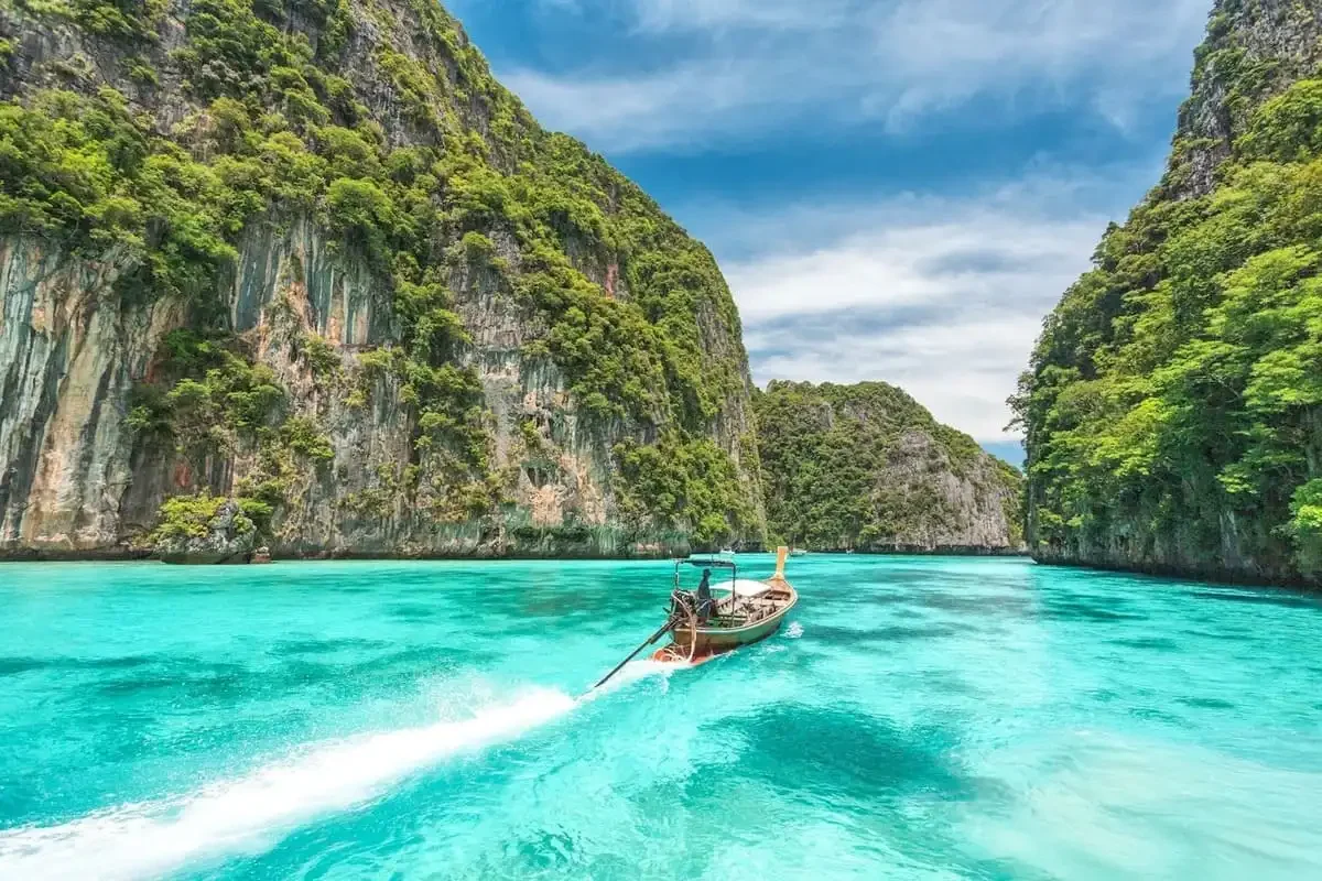 Longtail boat cruising through the emerald waters of Phi Phi Lagoon surrounded by towering cliffs.