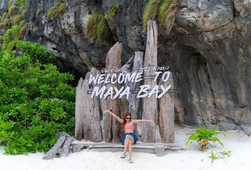Traveler relaxing in front of the “Welcome to Maya Bay” sign on the white-sand beach during a Phi Phi Islands private speedboat tour.