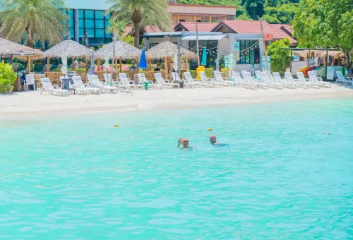 Visitors swimming in clear shallow water near a beachfront resort at Phi Phi Don.