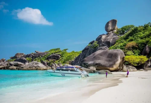 Private speedboat anchored at the white-sand beach of Similan Islands with famous Sail Rock