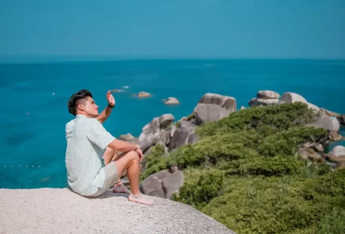 Traveler sitting at Similan Islands viewpoint overlooking blue ocean and boulders