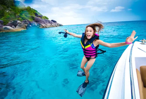 Excited young girl jumping from private speedboat into turquoise Similan Islands water