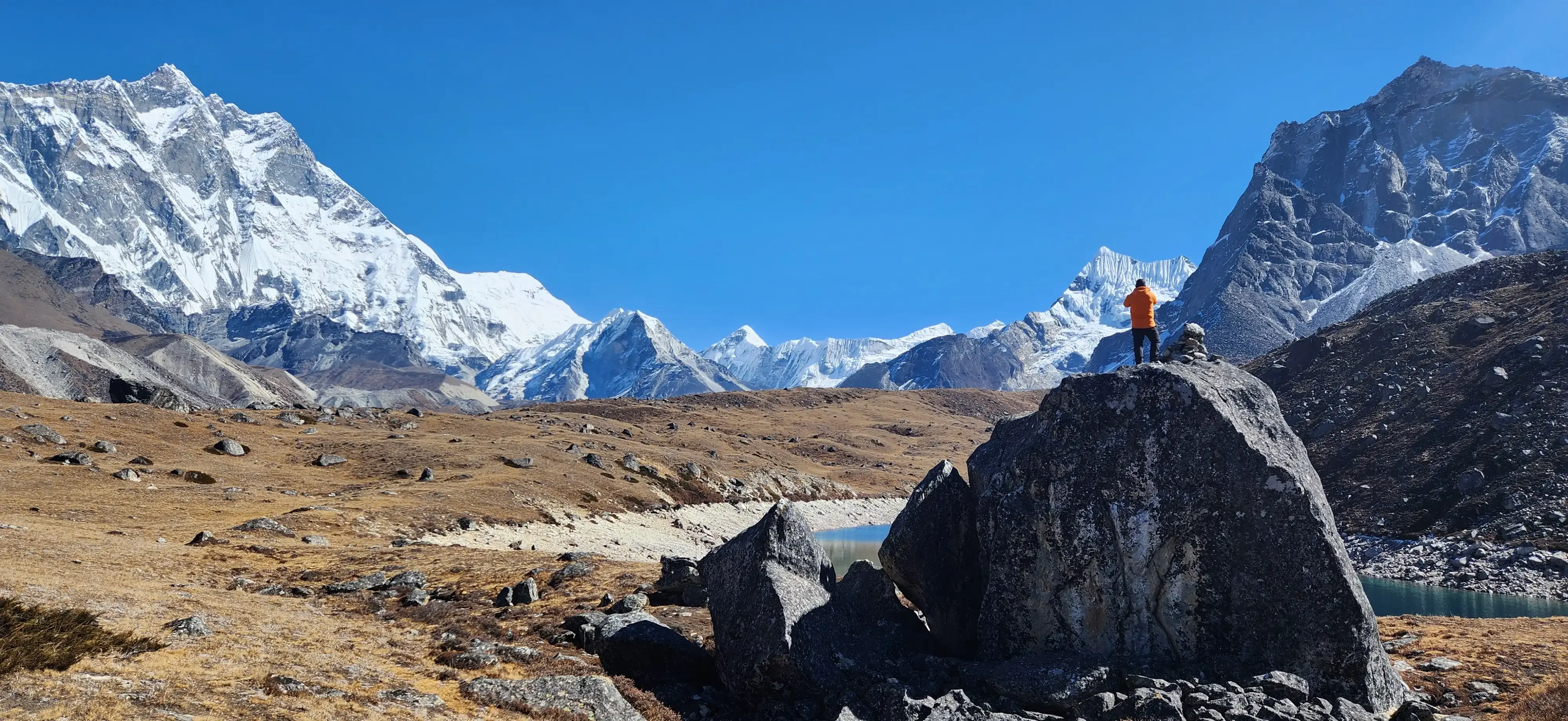 A person stands on a boulder on the way to Everest Base Camp overlooking the mountains in crisp Himalayan weather