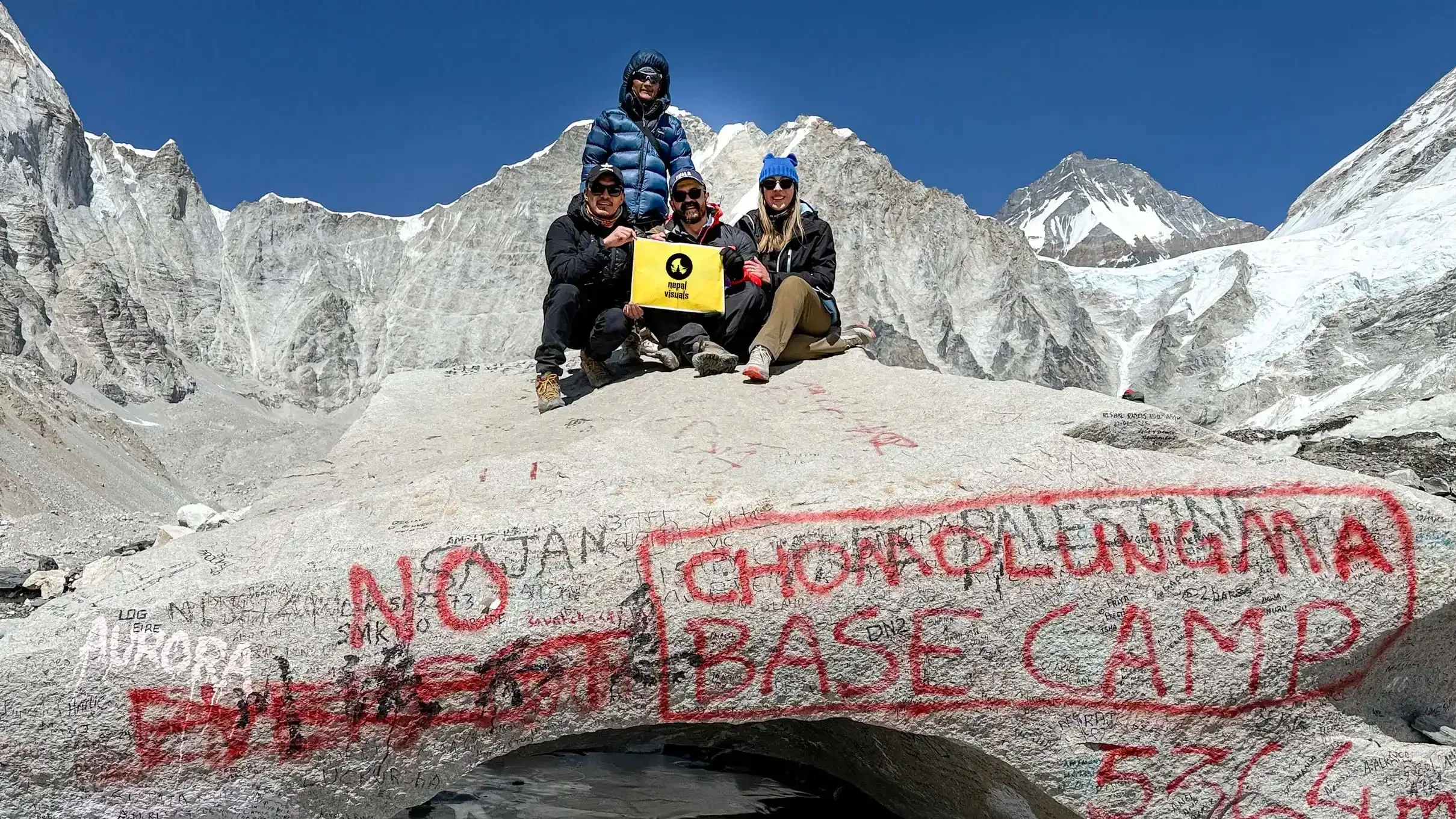 Trekkers celebrating in front of the iconic Everest Base Camp stone marker after completing the trek - Nepal Visuals